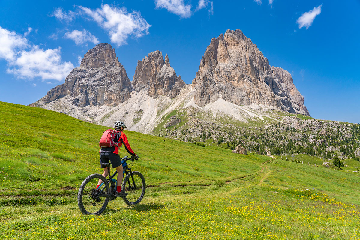 Ciclista in mountain bike sui prati alpini davanti al gruppo del Sassolungo nelle Dolomiti