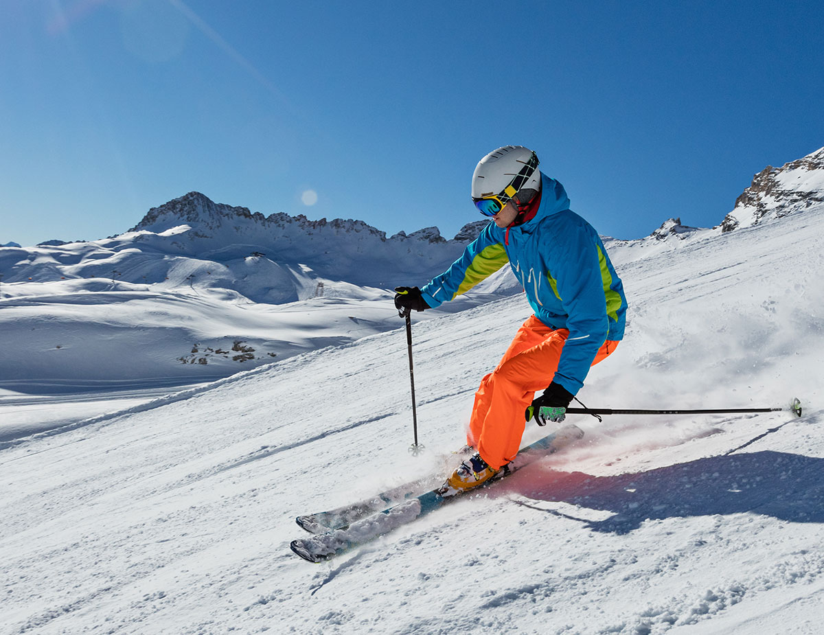Sciatore in curva su una pista battuta davanti a montagne innevate